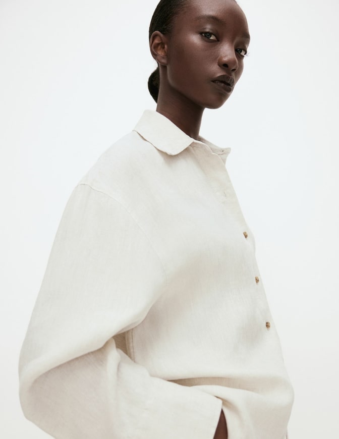 Portrait of a woman in a cream linen shirt with a collar, facing left against a pale background.